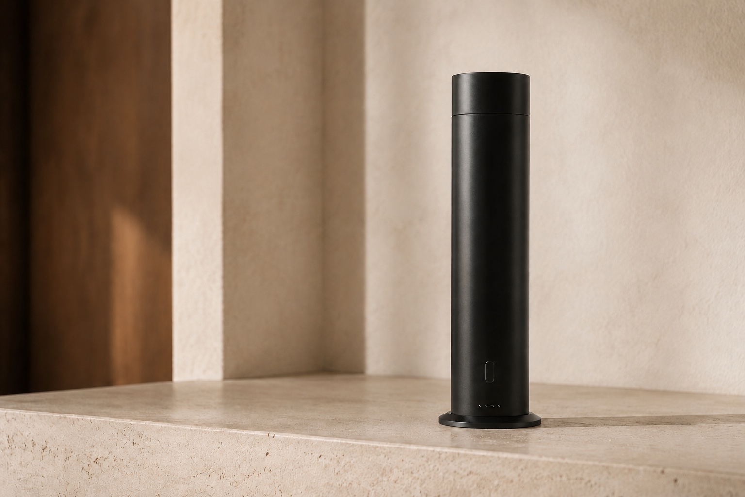 Black cylindrical waterless scent diffuser on a warm limestone surface in a refined interior.